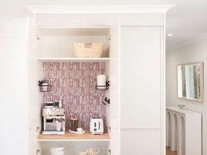 A picture of a white appliance cupboard with decorative adhesive tiles on one of the shelves in the room