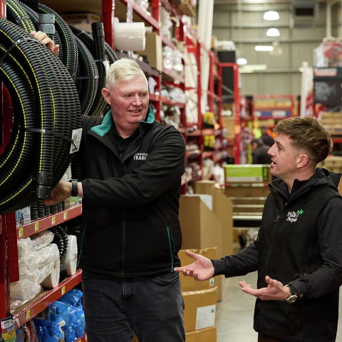 Bunnings Trade team member speaking with a customer beside a display of flexible hoses in a store aisle.