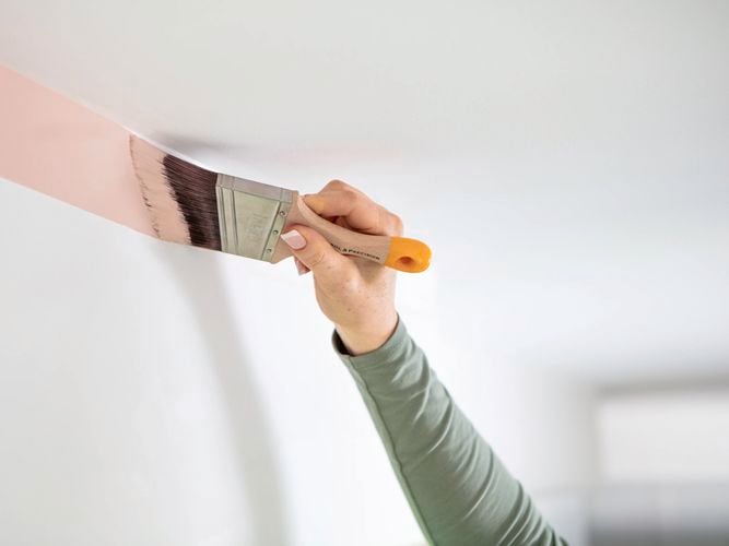 Person painting wall edge with a cutting in brush.