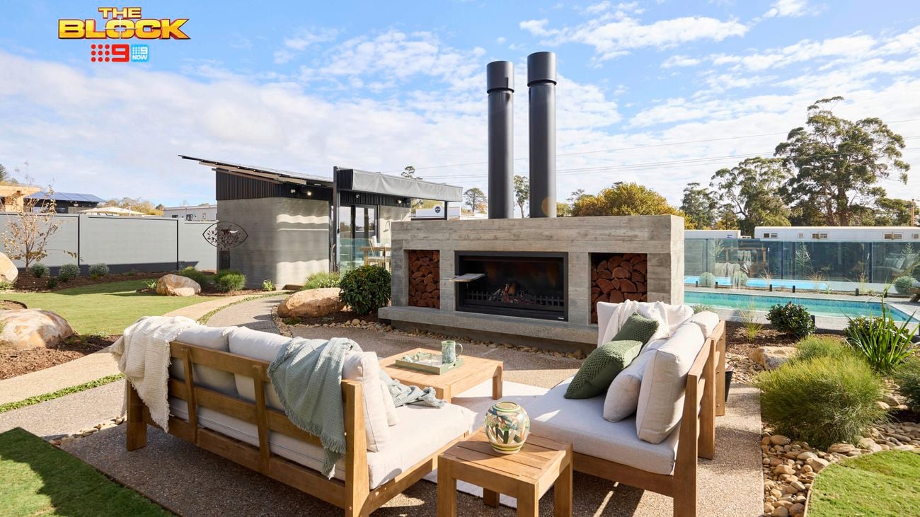An outdoor setting, with an outdoor fireplace, a pool with fencing around it, an outdoor room and plants in it.