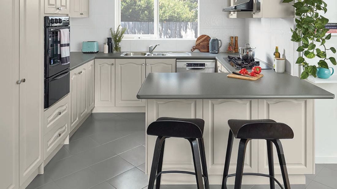 A kitchen with white painted cabinets, grey floor tiles and grey benchtops