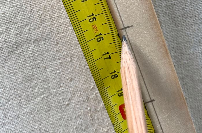 A person measures and marks evenly spaced vertical lines on a pine piece.