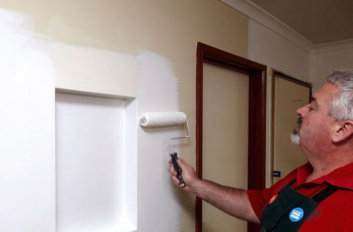 A man painting around a wall niche using a roller