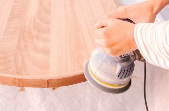 Hands using a sander to finish curved edges of wood plank.