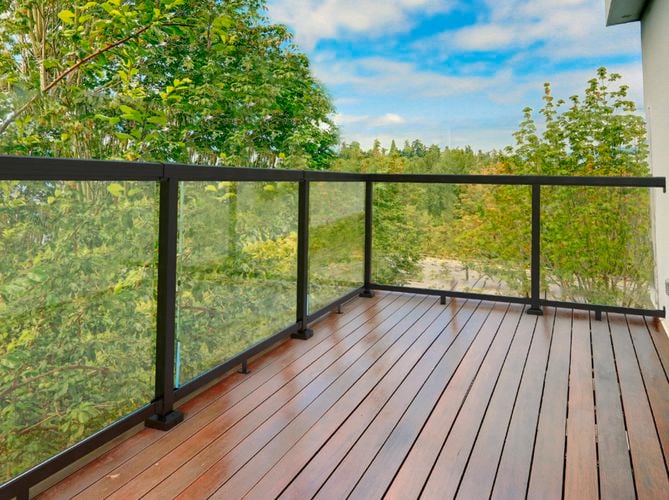 View from a balcony overlooking greenery, with a wooden balcony floor and a black aluminium balustrade.