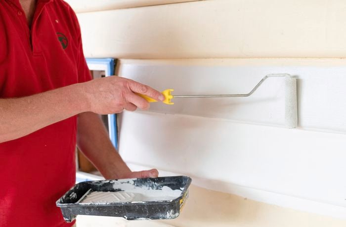 A person painting weatherboards with a small roller