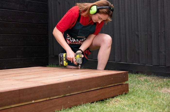 A Bunnings team member assembling decking outside a wooden shed