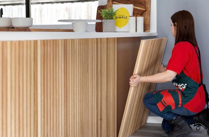 Person placing dowel timber feature wall in place underneath kitchen bench.