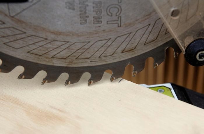 Closeup of a mitre saw blade lined up at a 45 degree angle against a plank of wood
