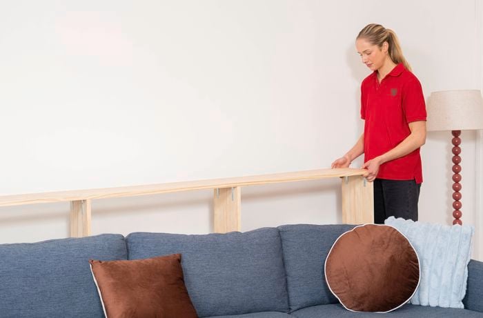 A Bunnings Team Member is placing timber shelf behind a couch