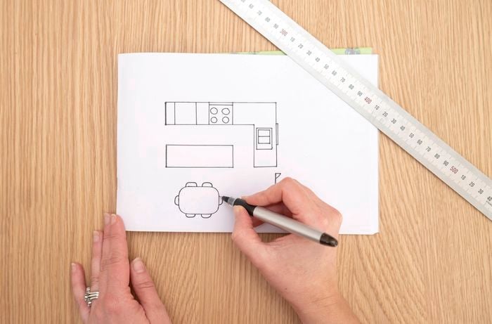 A person is sketching a simple kitchen floor plan on paper.