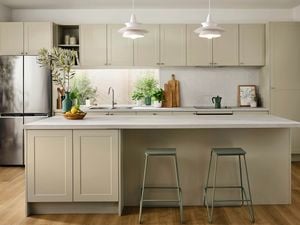 A modern New Rural kitchen featuring soft sage green shaker cabinets, light stone benchtops, timber flooring, and potted greenery for a fresh, natural look