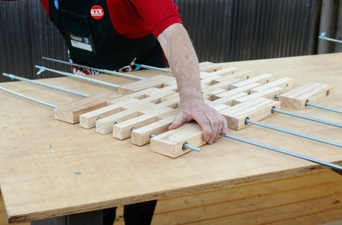 Person inserting metal poles in various pieces of wood in floor mat shape.