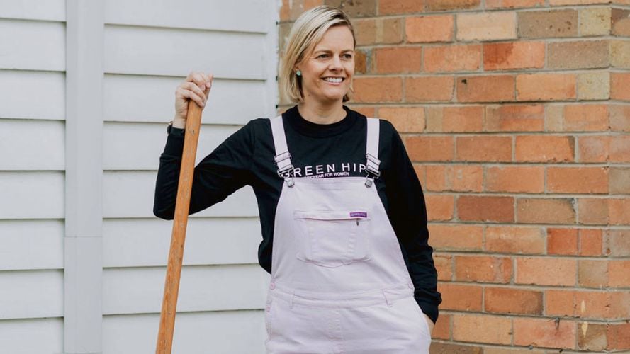 Lady wearing overalls and holding a long handle shovel.