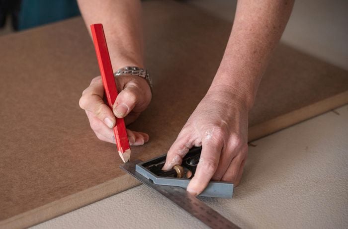 A person marking the cabinet door areas using a ruler and pencil.
