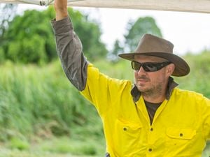 Three tradies talking on a frame and truss structure wearing high vis clothing and sun safety hats.]