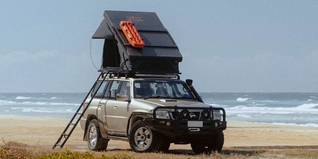 4 wheel drive vehicle with a roof tent attached, on the beach with the waves in the back ground