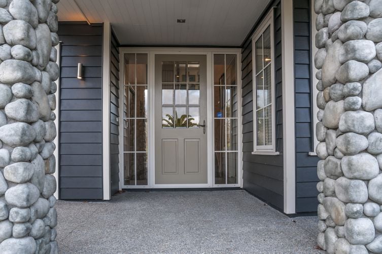 Front entryway to weatherboard home with stone columns and a beige front door