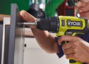 A woman wearing safety glasses and ear protection uses a green Ryobi cordless drill to fasten a screw into a cabinet