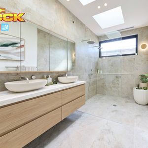 Modern bathroom with a floating timber double vanity, white vessel basins, large mirror, stone-look tiles and a spacious walk-in shower. “The Block” logo appears in the upper-left corner.