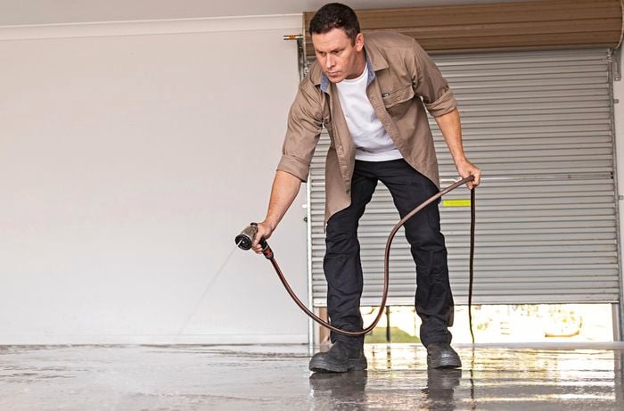 A man uses a hose to clean a garage floor