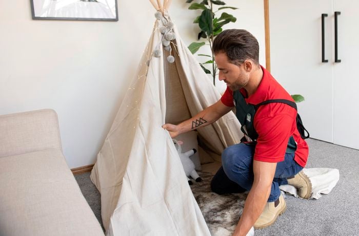 Person assembling DIY play tent in lounge room next to couch.