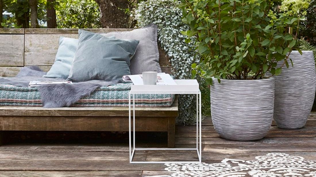 Outdoor setting with bench, cushions and lush green plants.