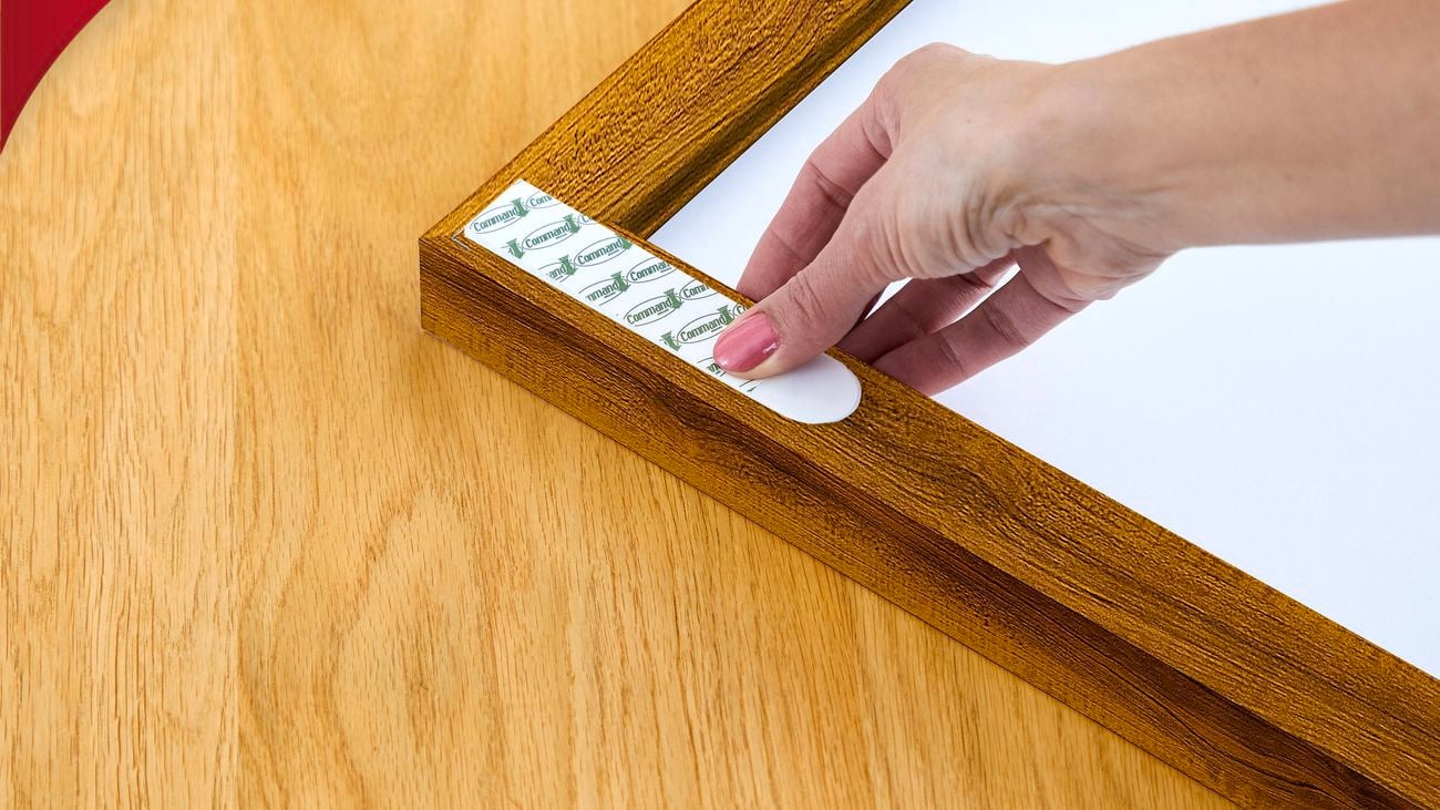 A person holding a strip of adhesive tape against a wooden frame