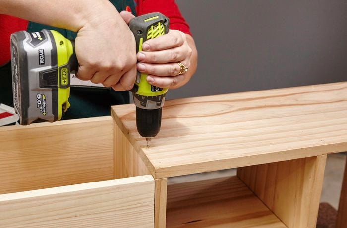 The top bench surface of a wooden storage bench being screwed down by a Bunnings team member