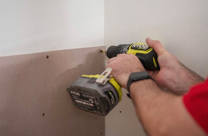 A person using a power drill to fasten a screw into a cement sheet.