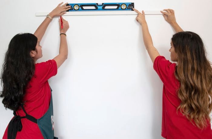 Two people holding spirit level against a wall.