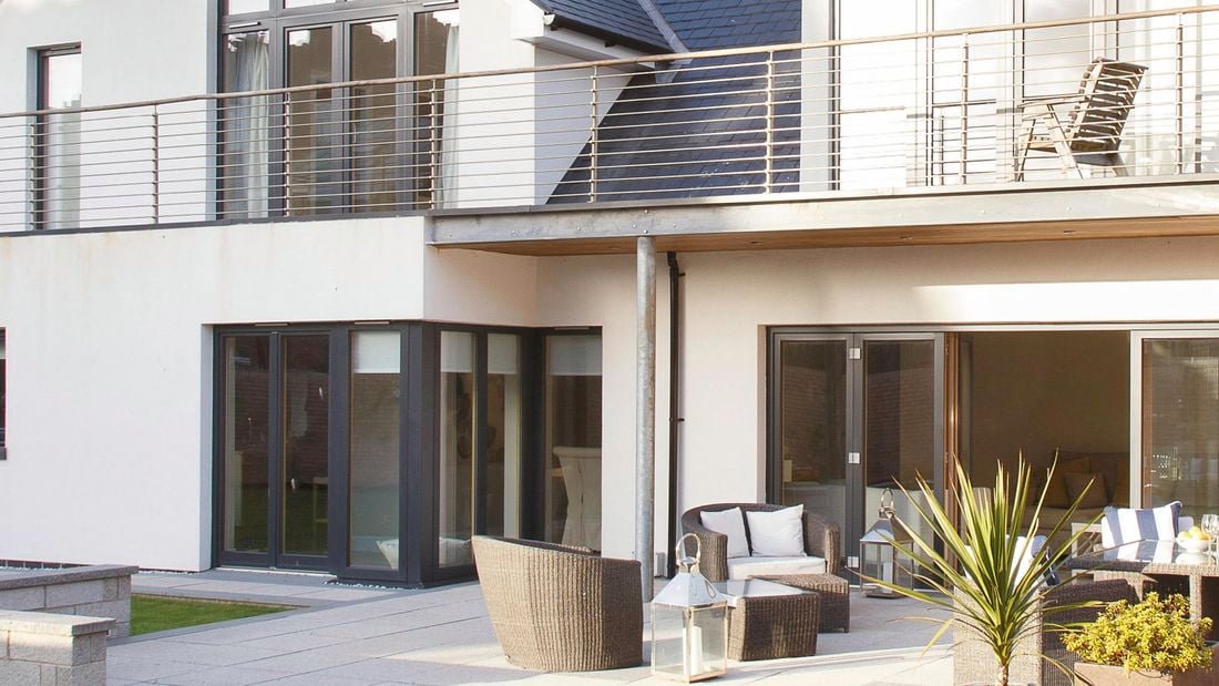 An outdoor area with wicker seating, lanterns, and a water feature underneath a second floor balcony with wire fencing