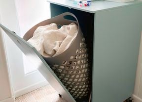 A light blue tilt-door laundry hamper cabinet with a grey hamper inside, holding white laundry.