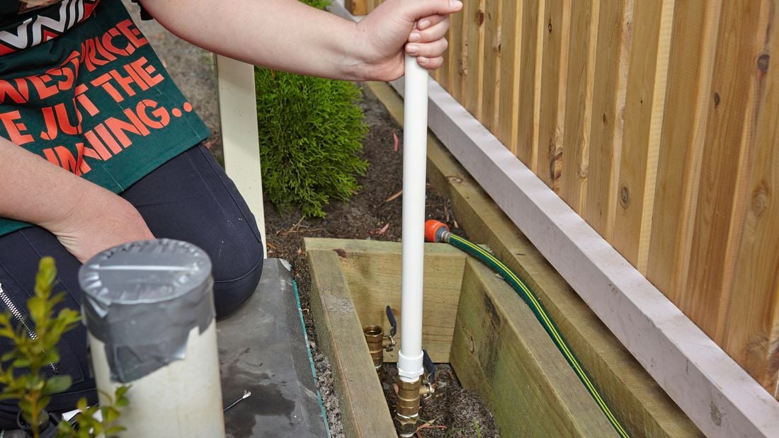Person sticking PVC pipe into dirt.
