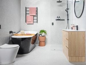 Bright bathroom with black bath tub, towel rail and tapware and terrazzo shower wall and toilet.