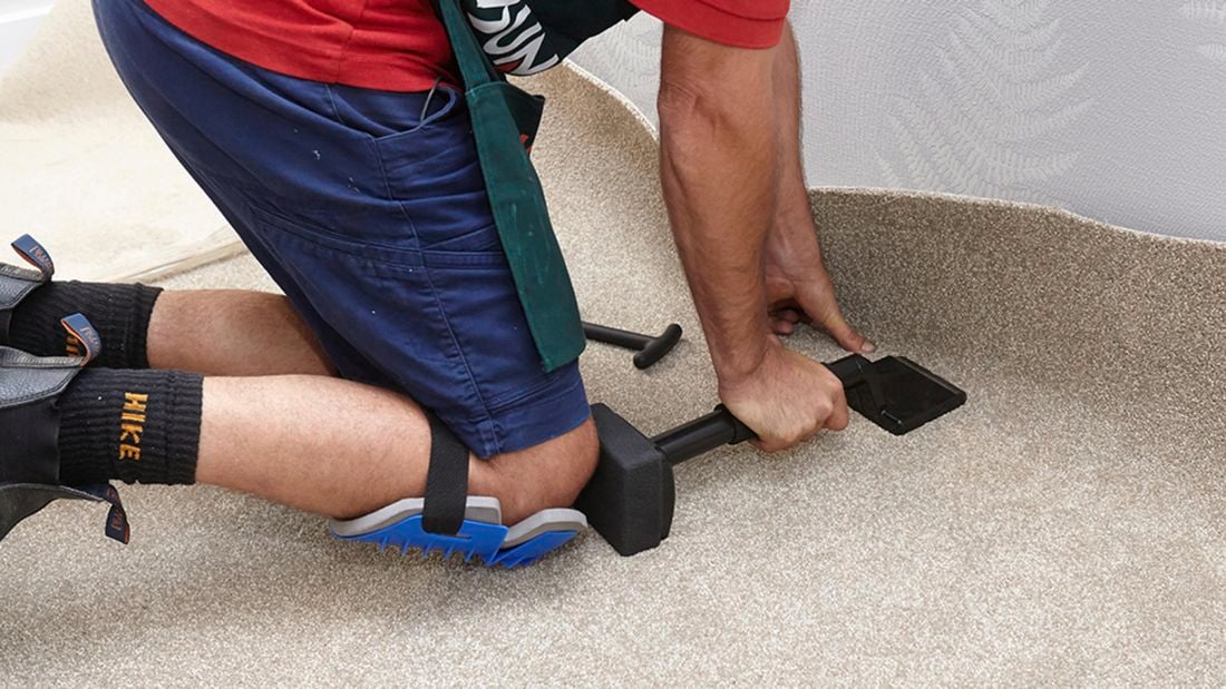 A knee kicker being used to push carpet into the corner of a room