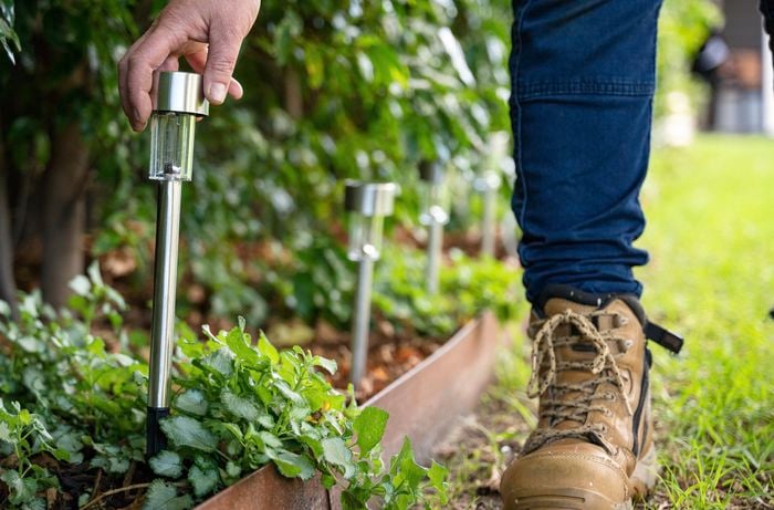 A person adding pathway lights to the garden.