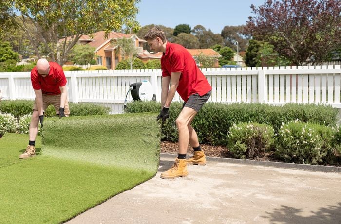 Two Bunnings Team Members are unrolling synthetic turf onto a prepared area.