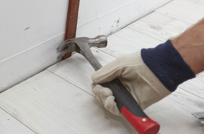 Person using hammer to remove skirting board nails.