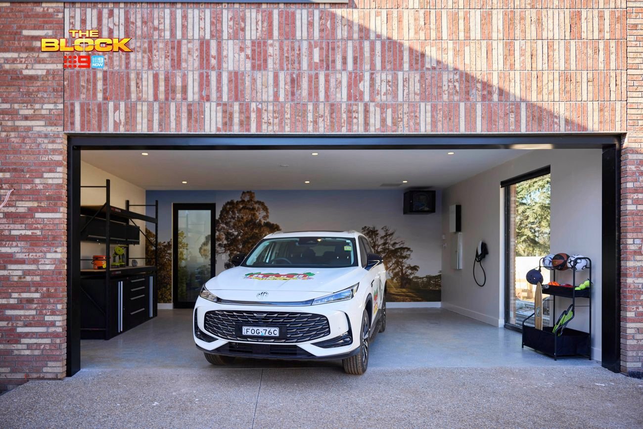 Garage from The Block with brick exterior, black cabinetry, wall mural, and white SUV parked inside.