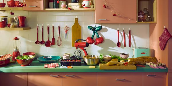 3M Command Hooks used to organise kitchen utensils, decorations and oven mitts on a tiled splashback above a kitchen benchtop.