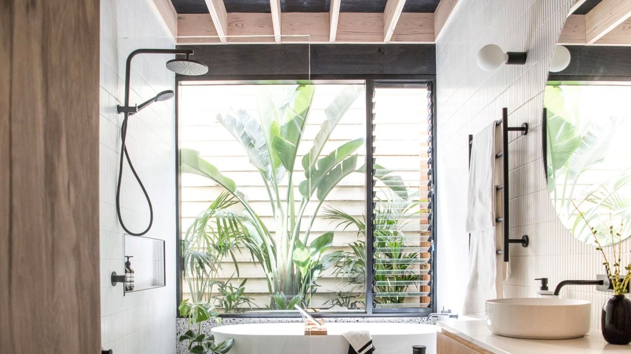 Shot of modern bathroom with tiled floor, white bathtub in background near window and black shower head in midsection.
