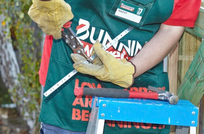 A Bunnings team member cutting a fix strip to size with tin snips