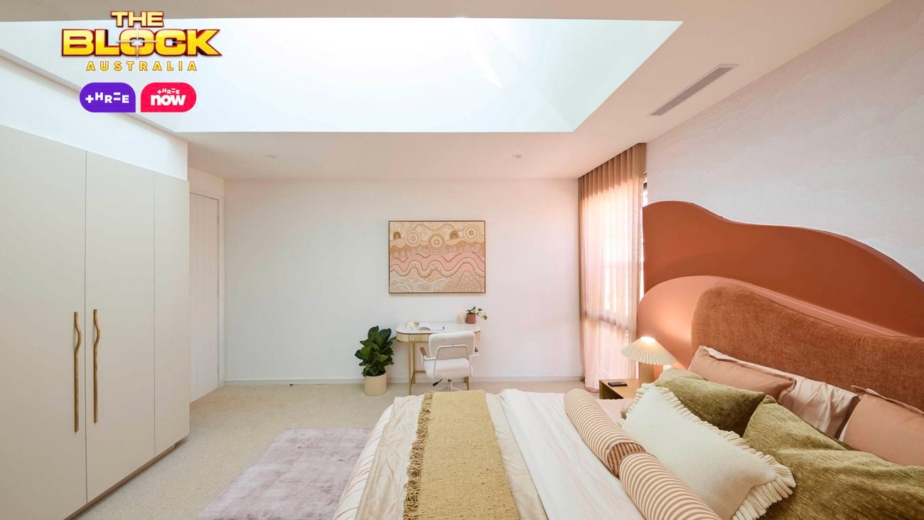 Cream bedroom with a queen bed, desk and wardrobe on a blush rug and a red and orange hill style bedhead.