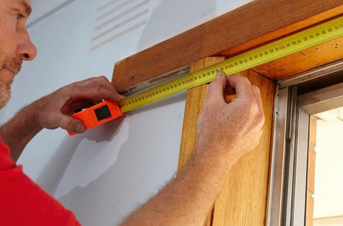 Person using measuring tape to measure window frame.