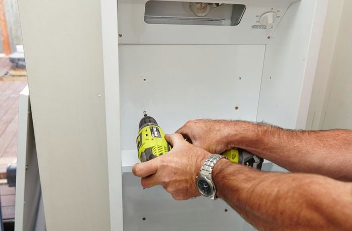 Using the drill and screws to secure the ironing centre to the wall.