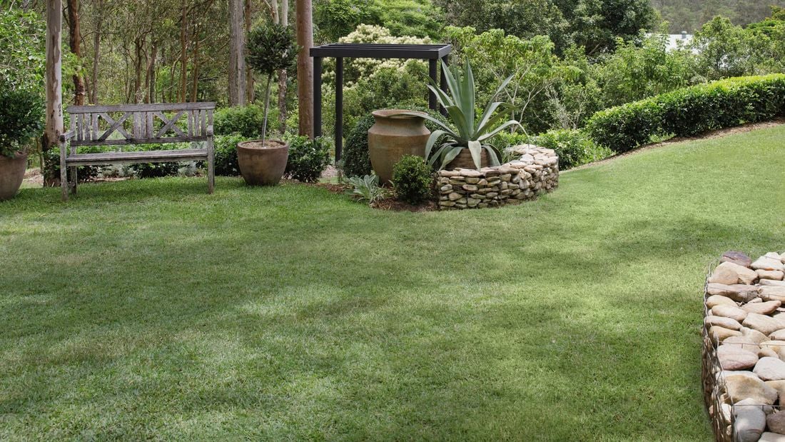 Backyard with green lawn, rocks, outdoor furniture and trees.