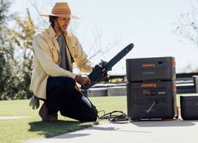 A man on the ground with a chainsaw, a Jackery solar generator and battery system beside him