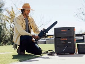 A man on the ground with a chainsaw, a Jackery solar generator and battery system beside him