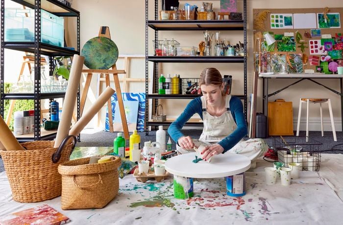 Bella in an art studio pouring teal paint onto round canvas
